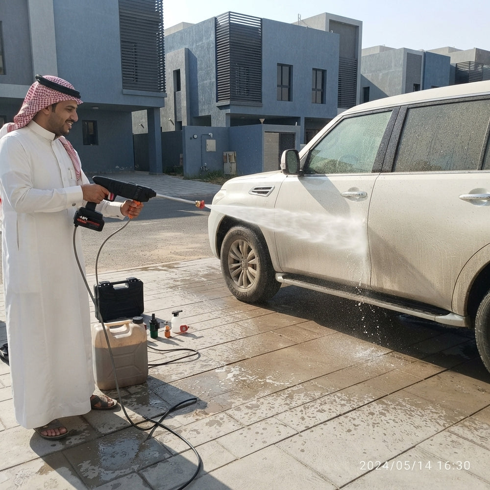 A person using a portable cordless pressure washer to clean a car in a sunny outdoor setting.